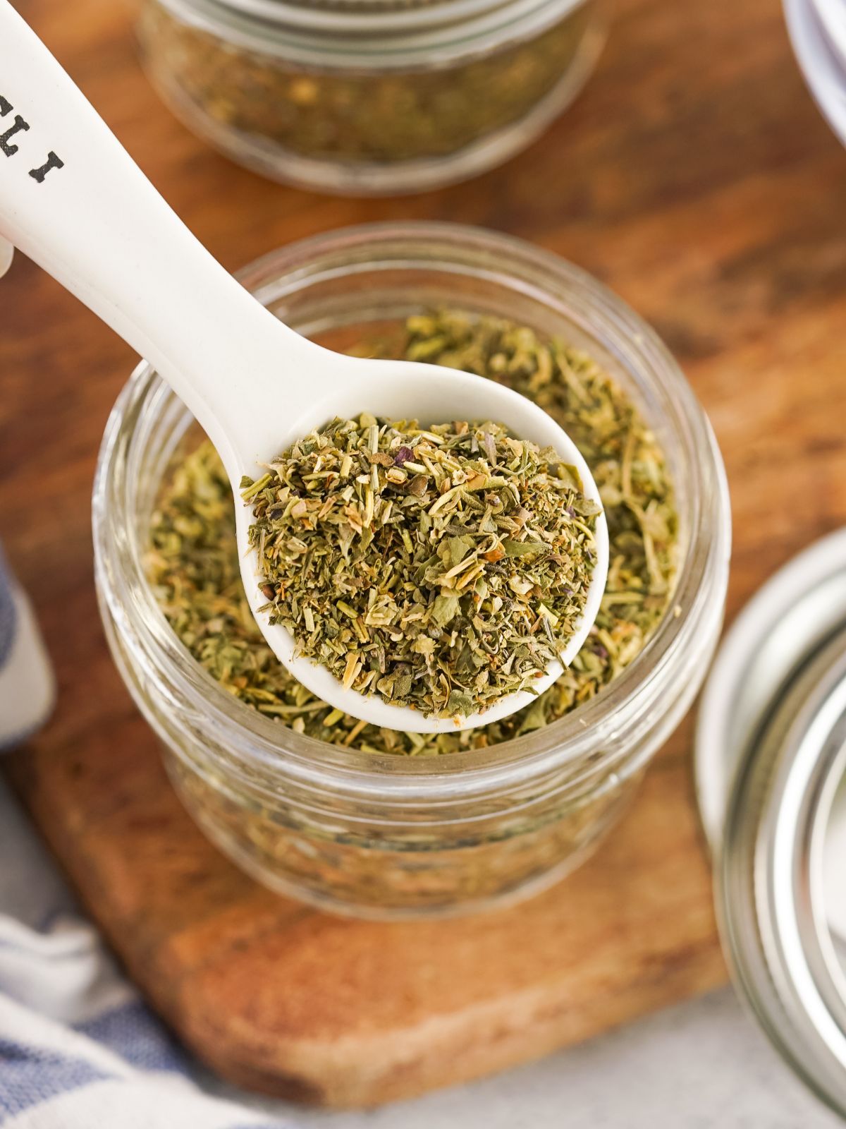 mason jar with Italian seasoning with white teaspoon.