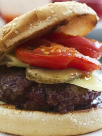 grilled burger on a sesame bun with tomato, pickle and cheese.