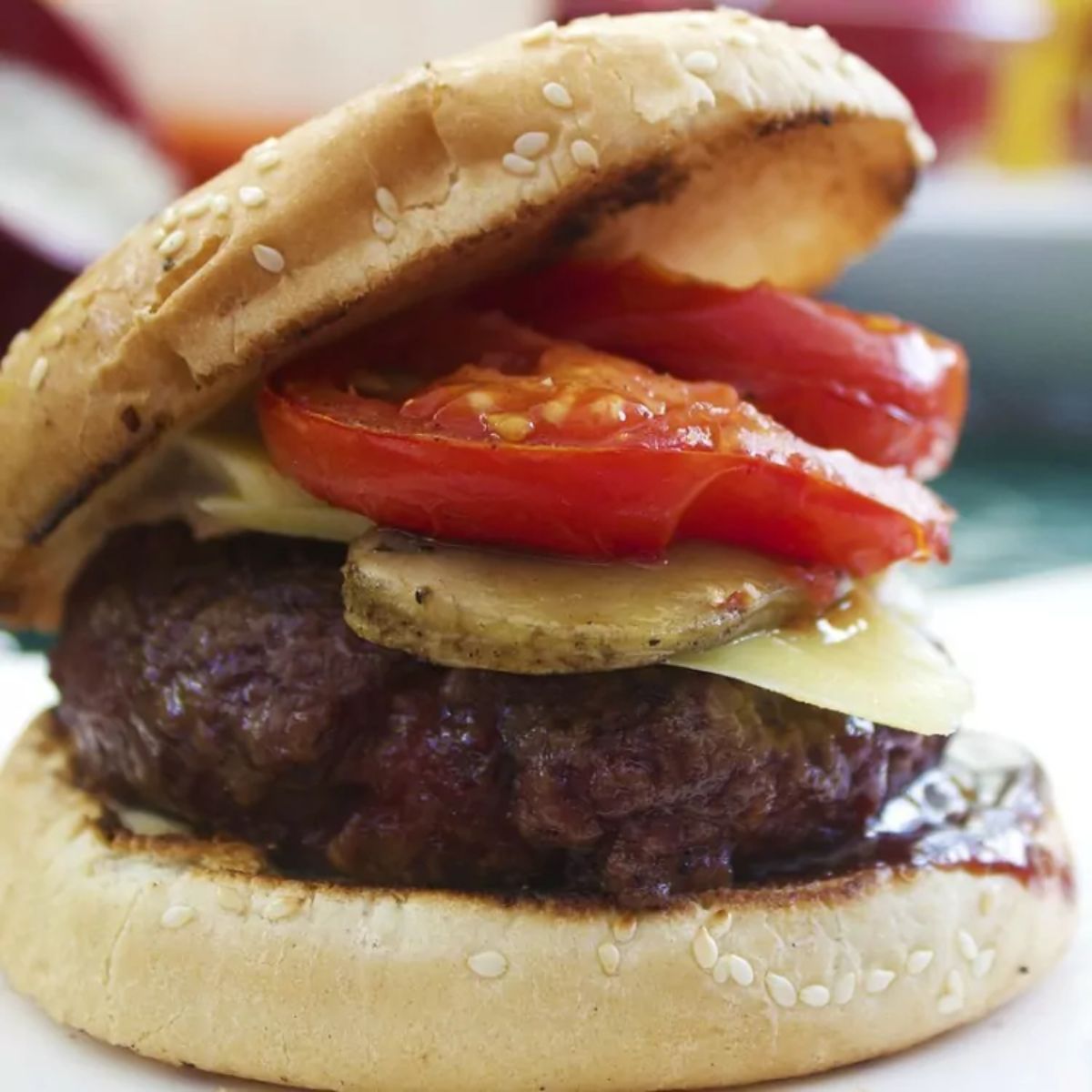 grilled burger on a sesame bun with tomato, pickle and cheese.