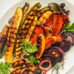 Pinterest vegetables with grill marks and fresh herbs on platter.