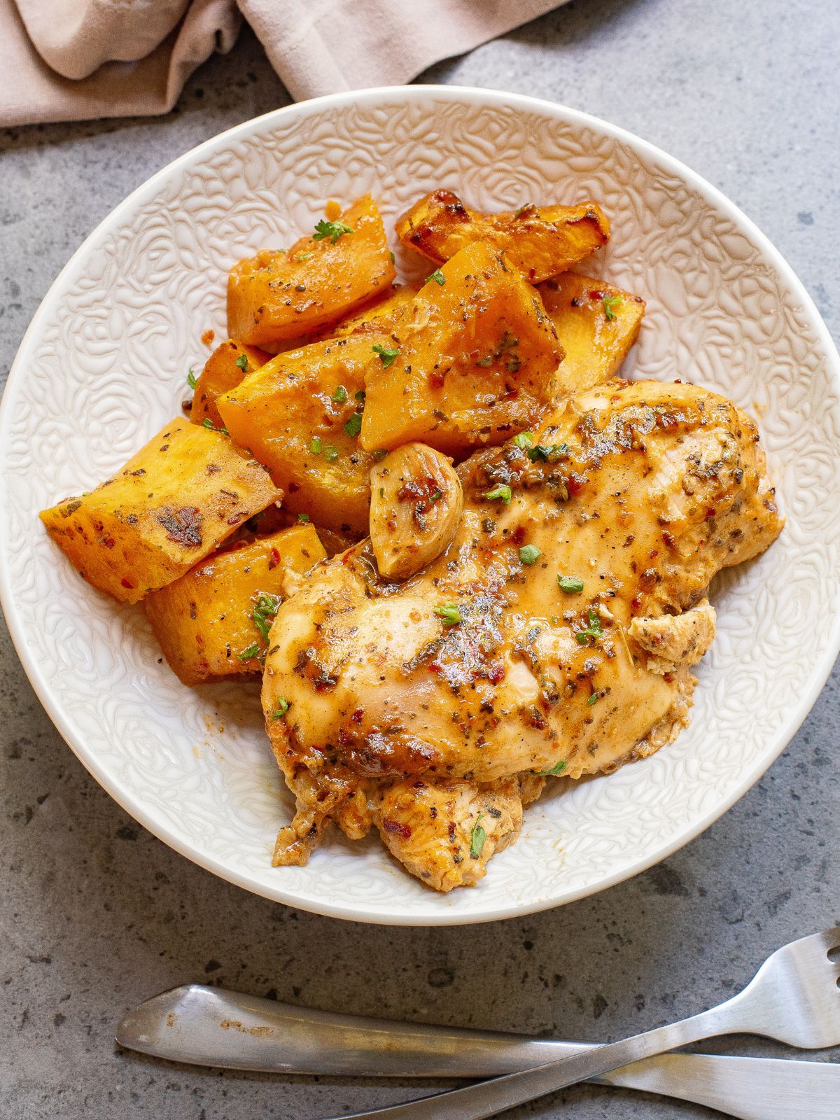 easy dinner recipe of chicken with butternut squash on white plate with fork and knife.