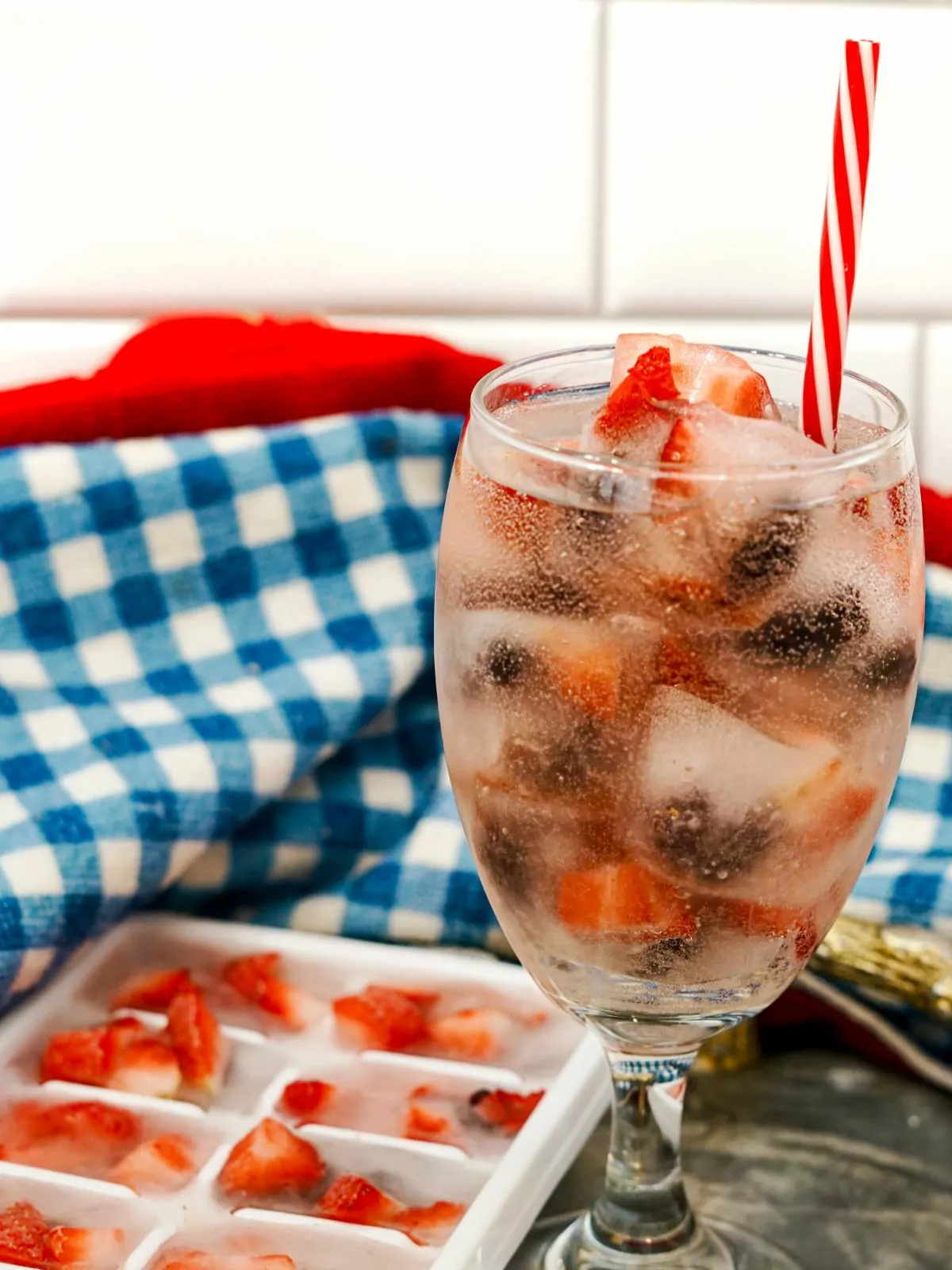 a glass of water filled with ice cubes with frozen fruit.