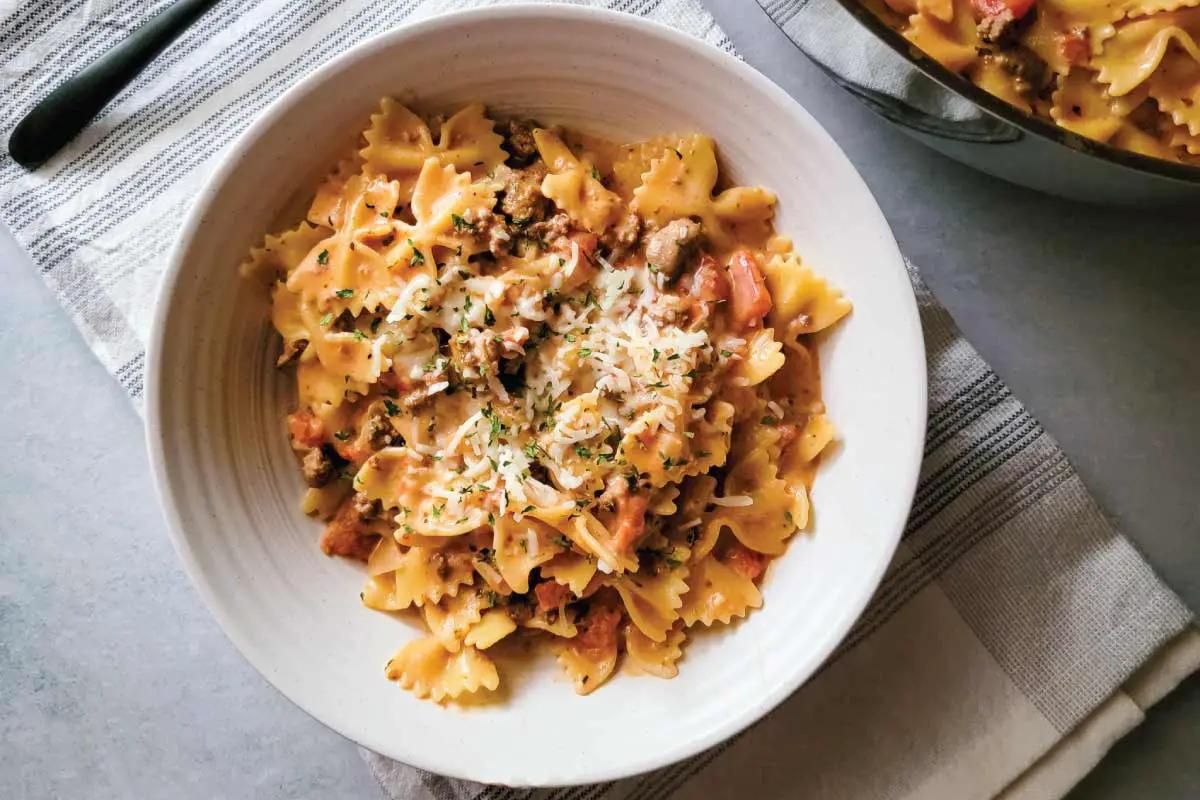 beef and bow tie pasta served in bowl with Parmesan cheese.