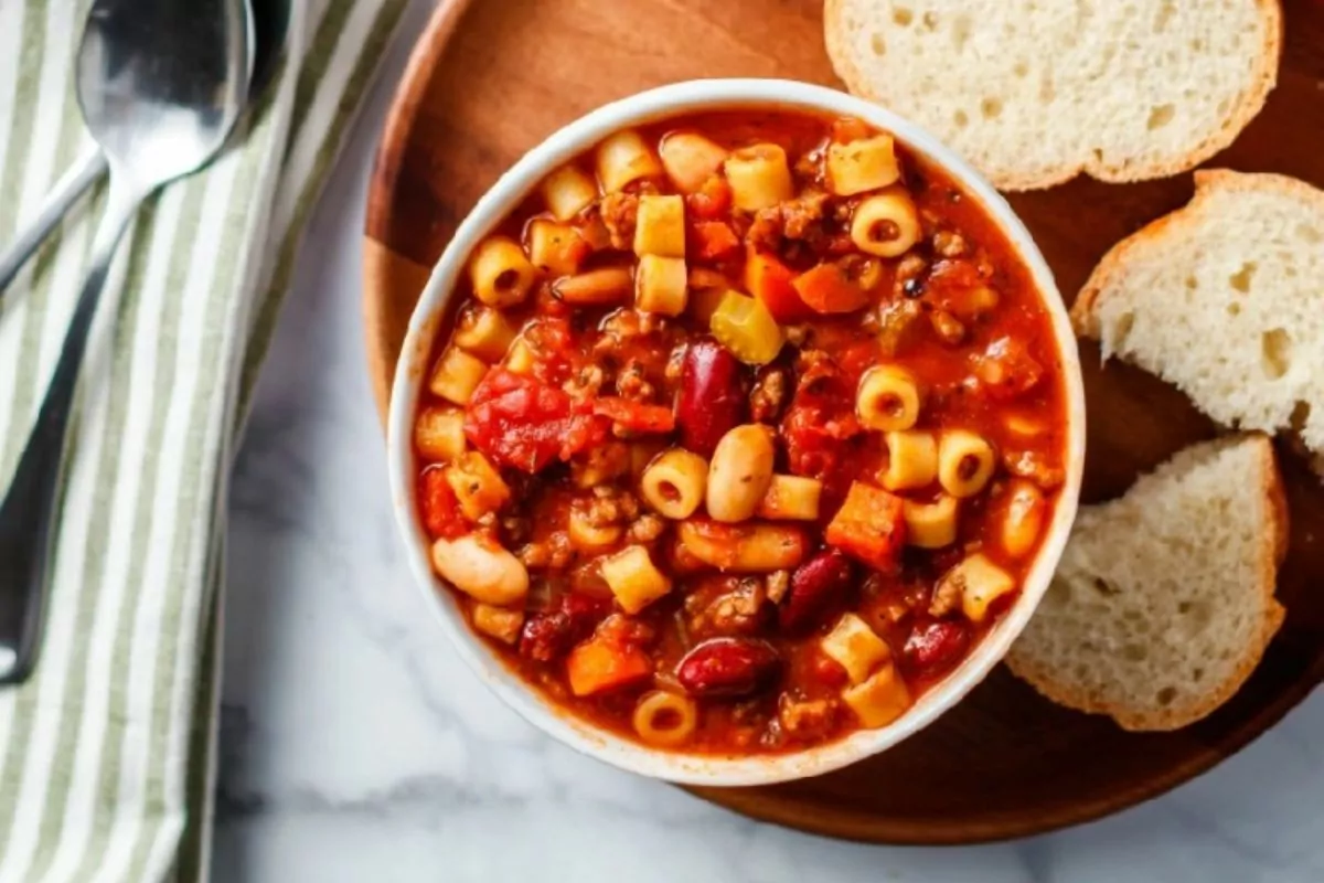 bowl of soup with pasta, beans, tomatoes and beef served with bread.