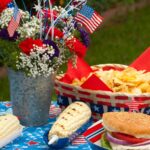 picnic table set with food and a bucket of flowers for patriotic holidays.