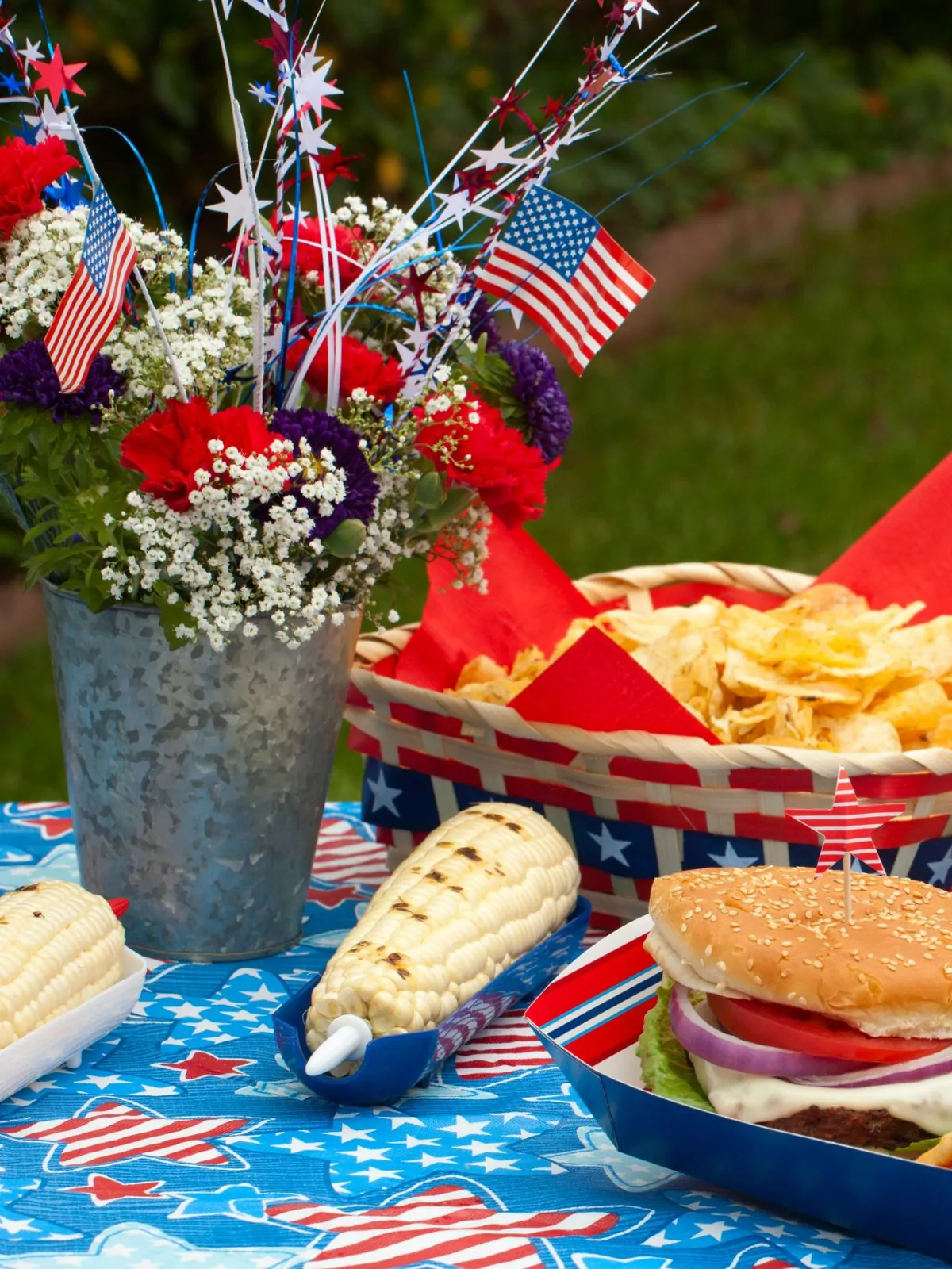 picnic table set with food and a bucket of flowers for patriotic holidays.