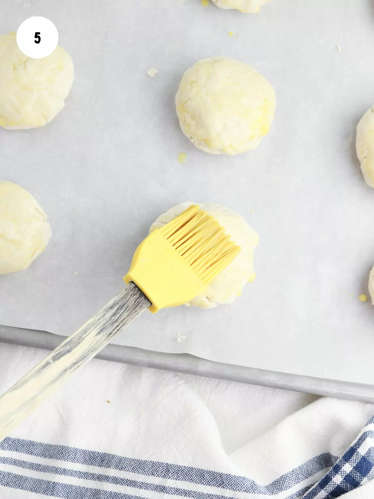Yellow pastry brush painting egg wash onto dough balls