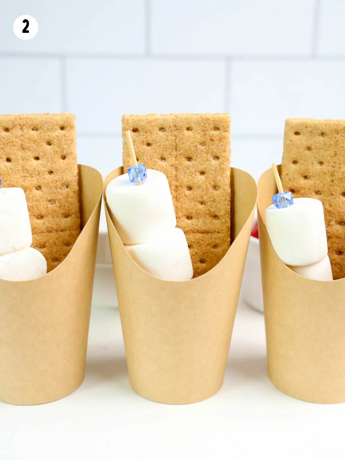 graham crackers with marshmallows on a stick in a paper cup.