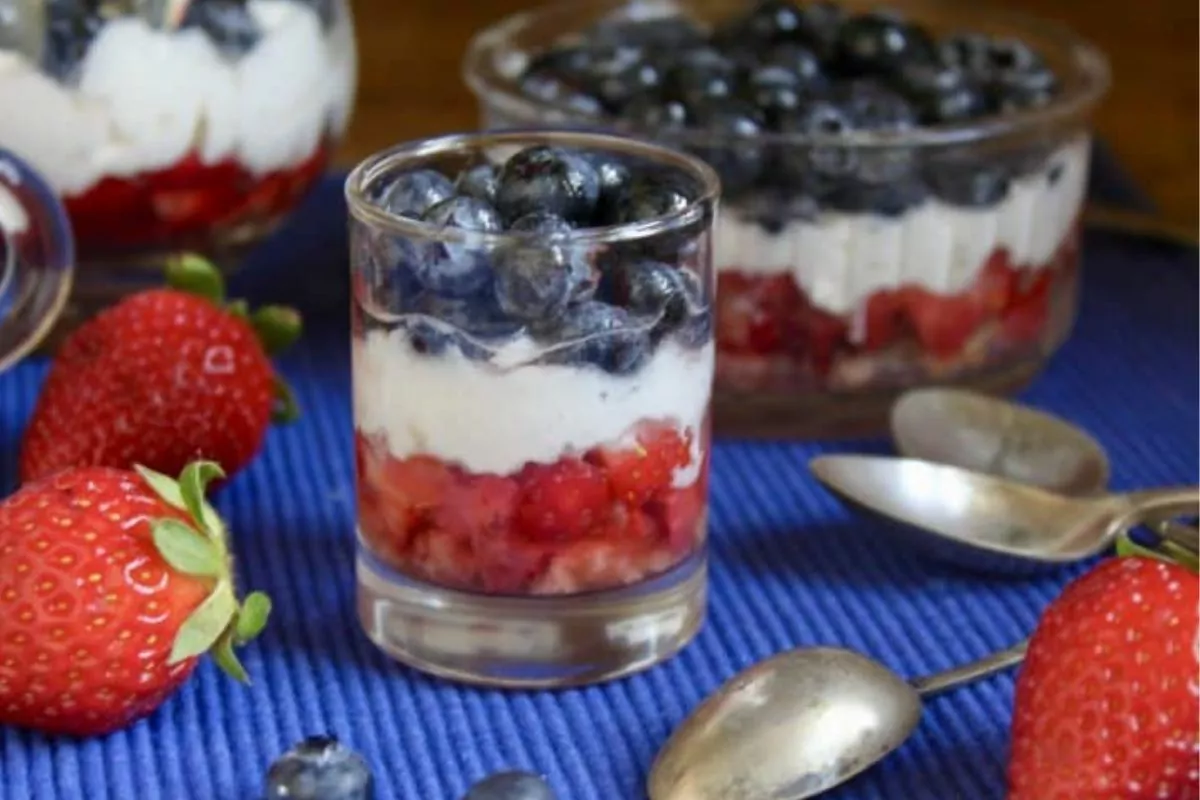 glass filled with strawberries, whipped cream and topped with blueberries.