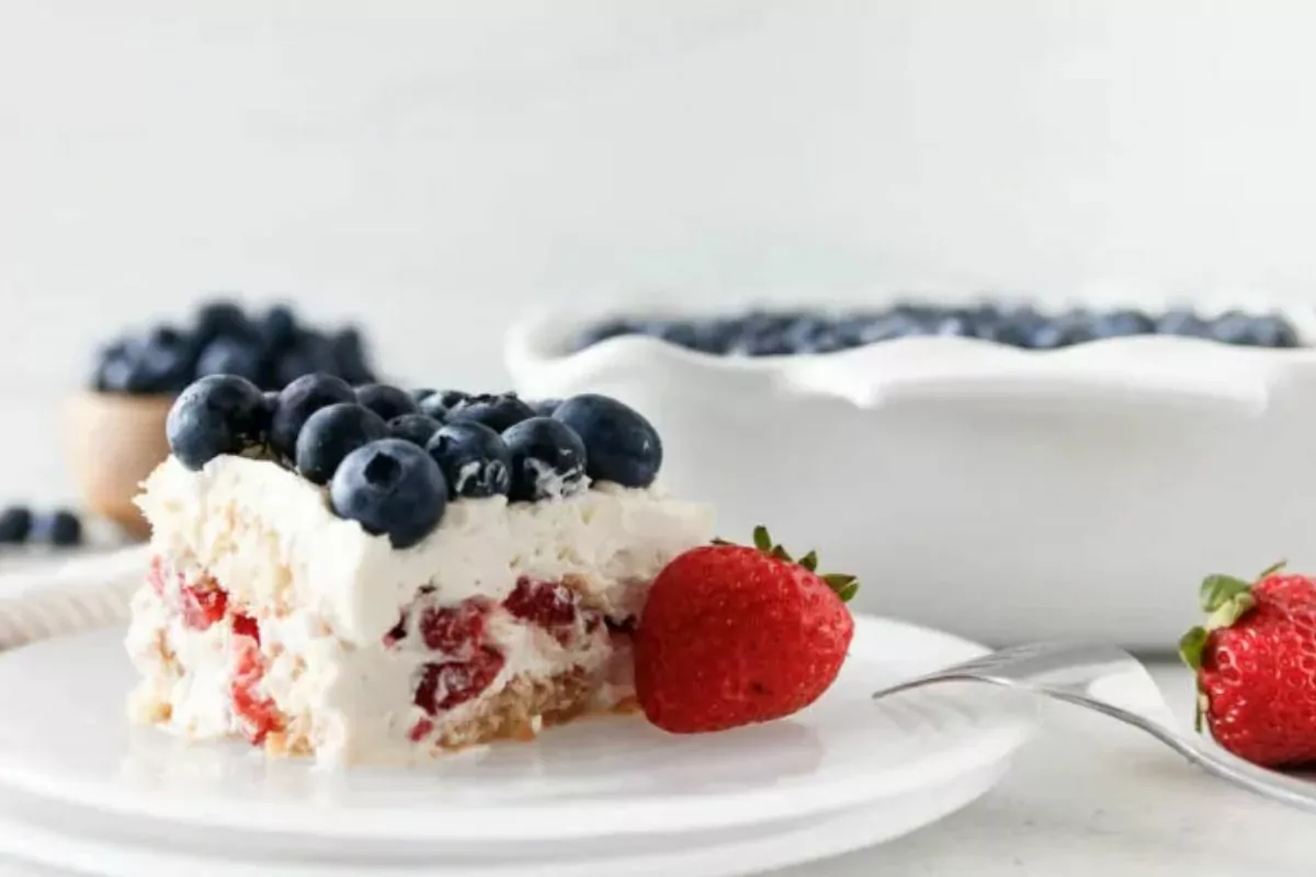 dessert on a plate with graham cracker crumb crust, whipped cream, strawberries and blueberries.