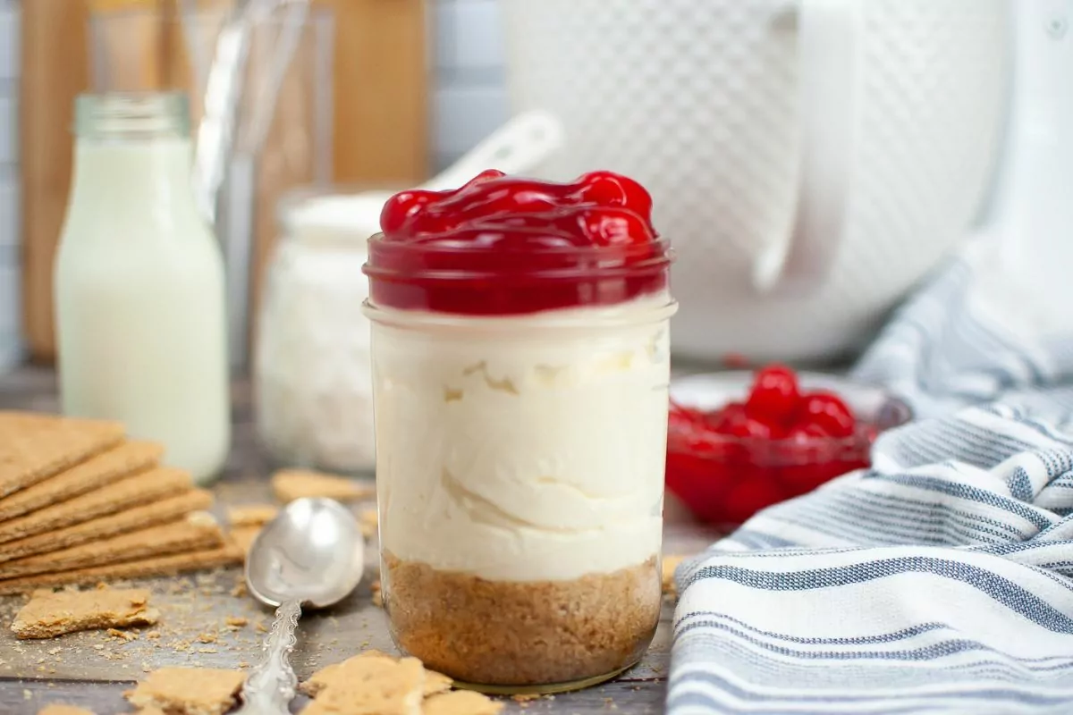 jar layered with crust, Cool Whip and Cheesecake Pudding, and cherry pie filling on top