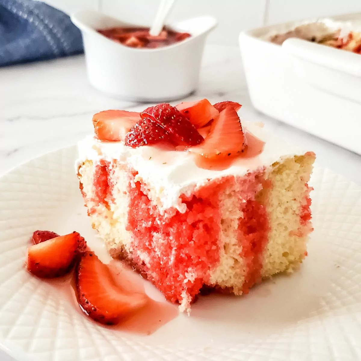 FEATURED Strawberry Poke Cake served on a white plate with fresh strawberries on top.