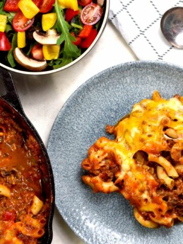 beef and noodle casserole served on plate and in skillet to the side with small bowl of salad.