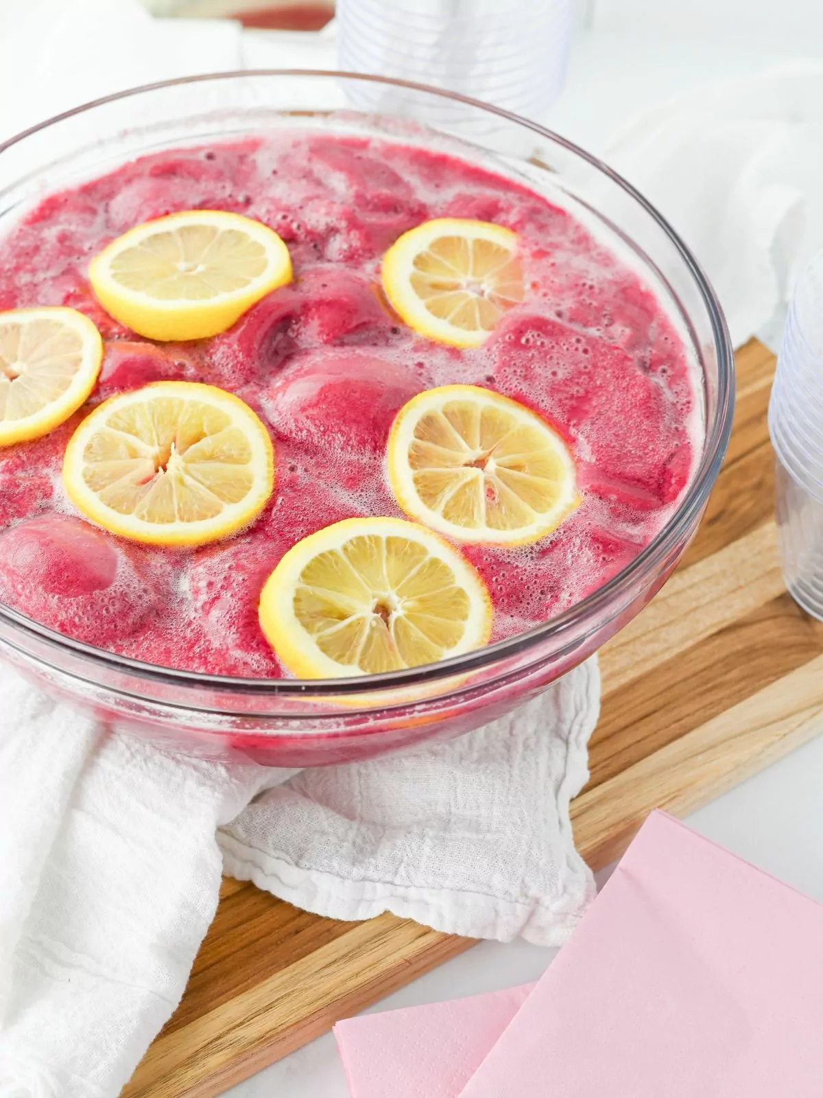 clear punch bowl filled with pink punch and lemon slices on a wooden cutting board