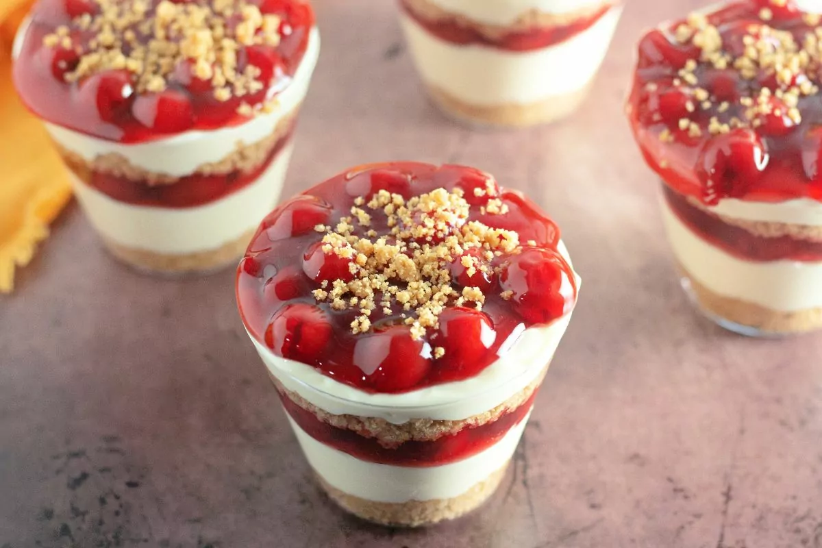Layered pudding with graham cracker crumbs and cherry pie filling in cups.