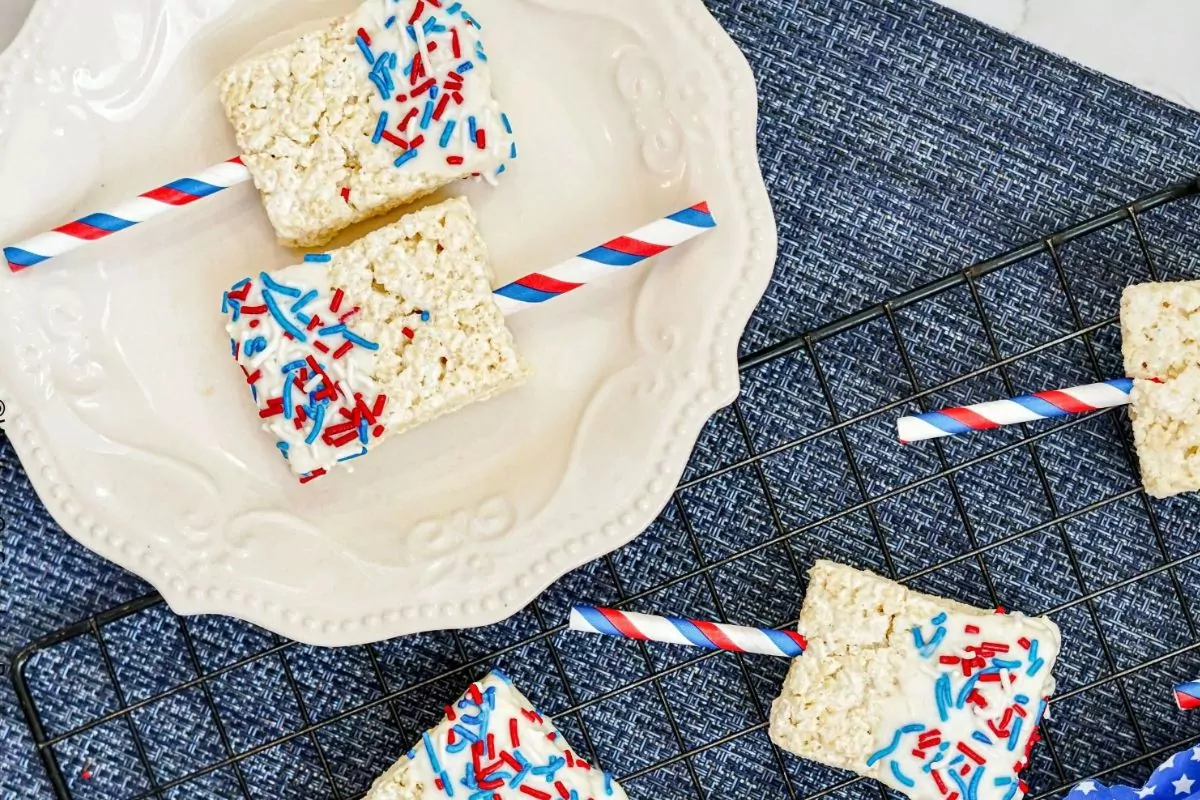 rice krispie treats dipped in melted chocolate and sprinkles with red, white and blue straws.