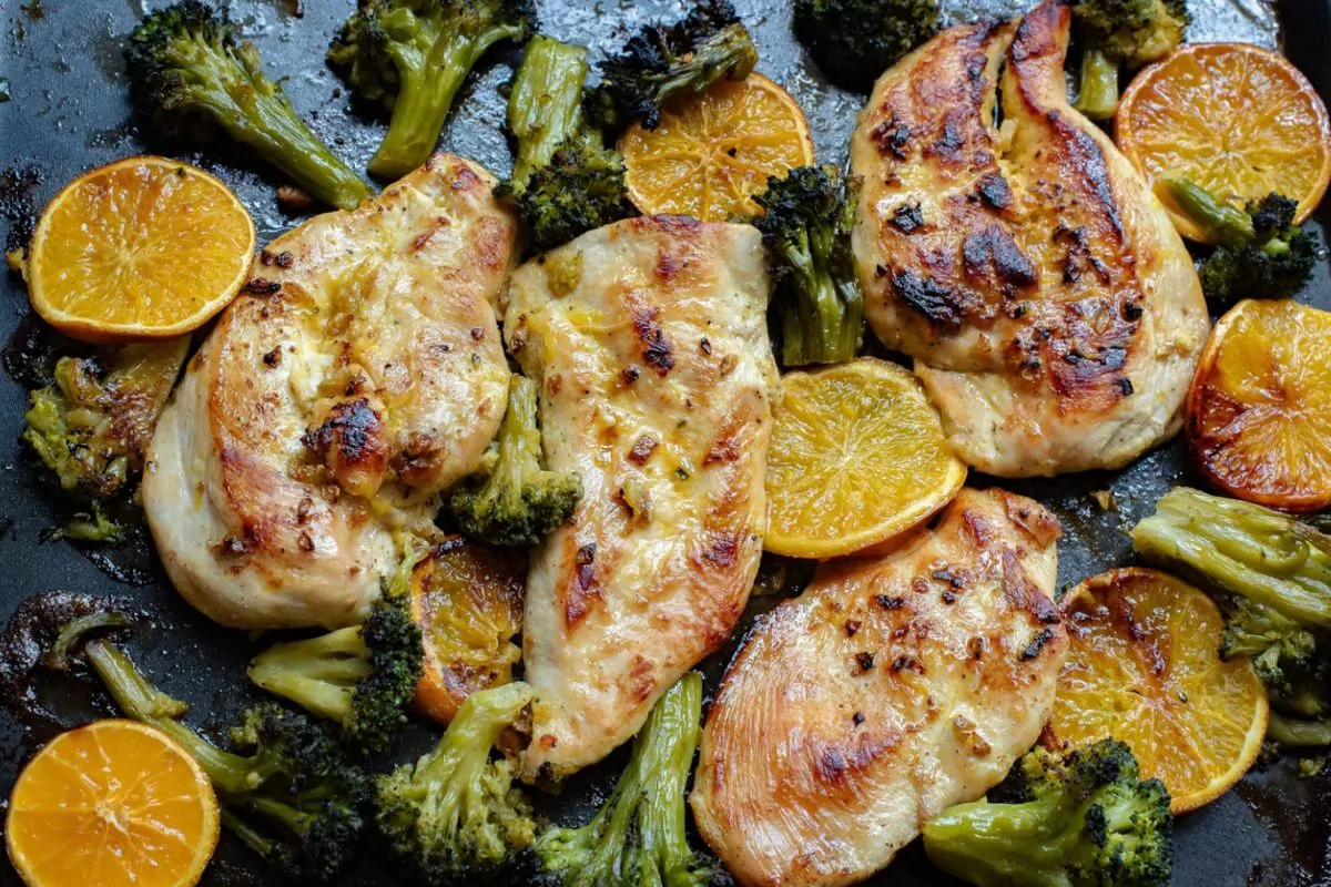 chicken with broccoli and orange slices baked on sheet pan.