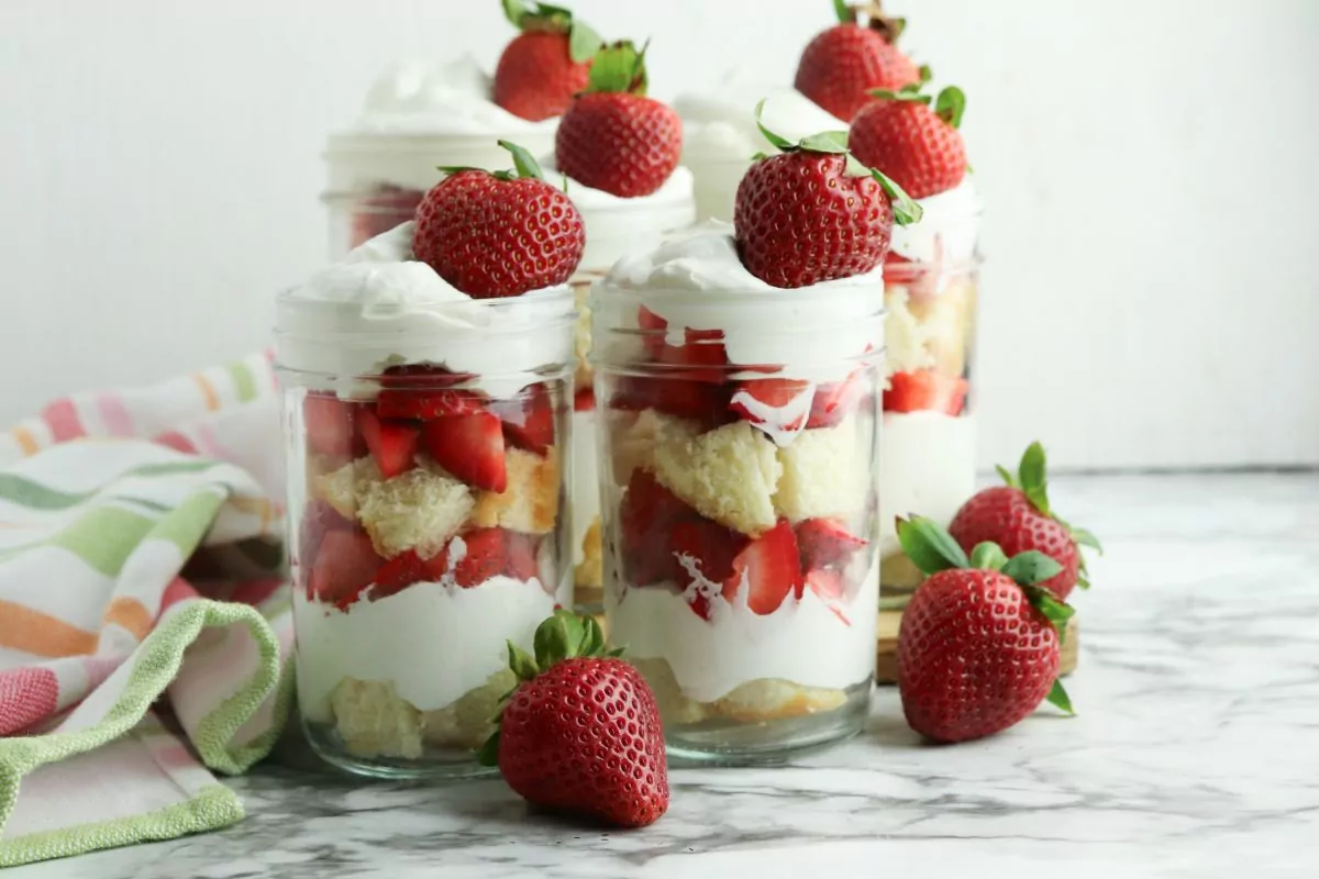 Strawberry Shortcake for MSN in mason jars with whole strawberries scattered around.