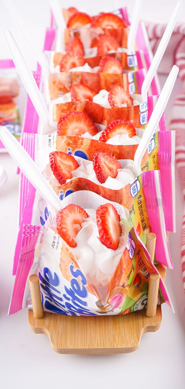 A close-up of a plastic bag filled with muffins topped with strawberry pie filling, whipped cream, and fresh strawberry slices.