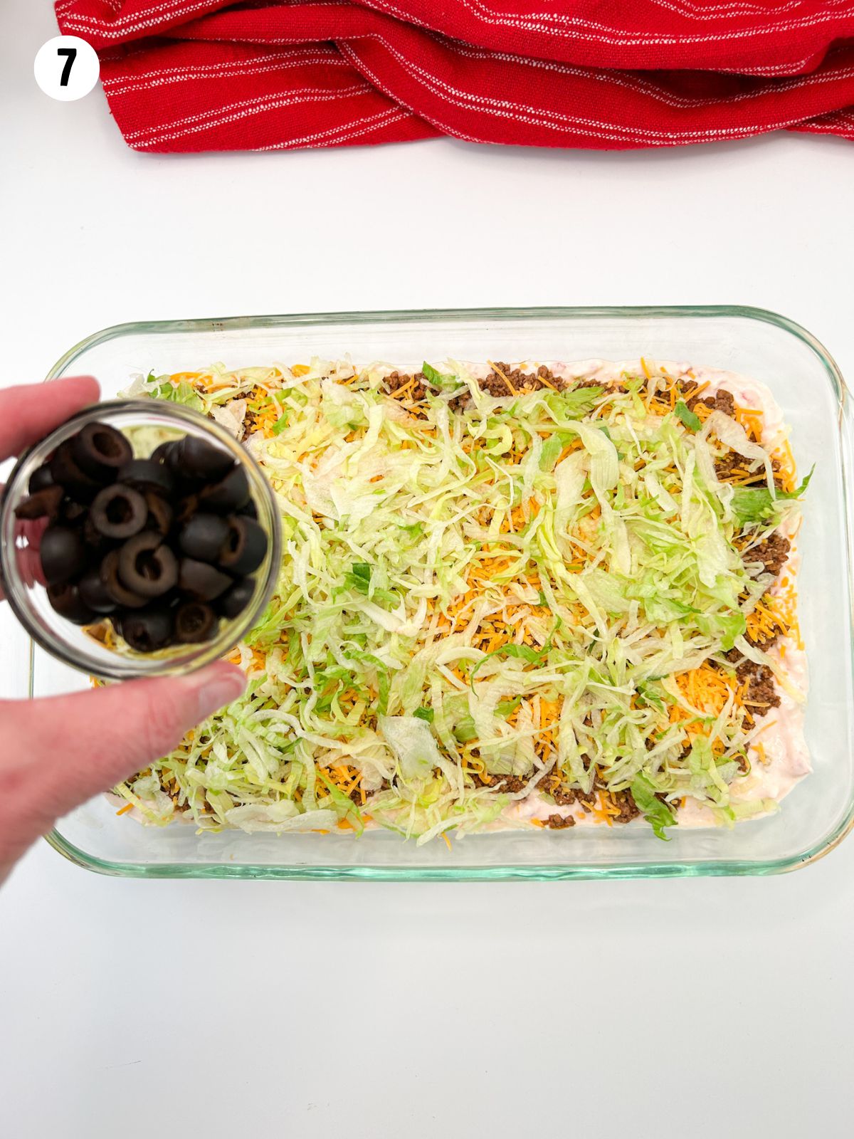 small bowl of olives being held over taco salad mixture in casserole dish.