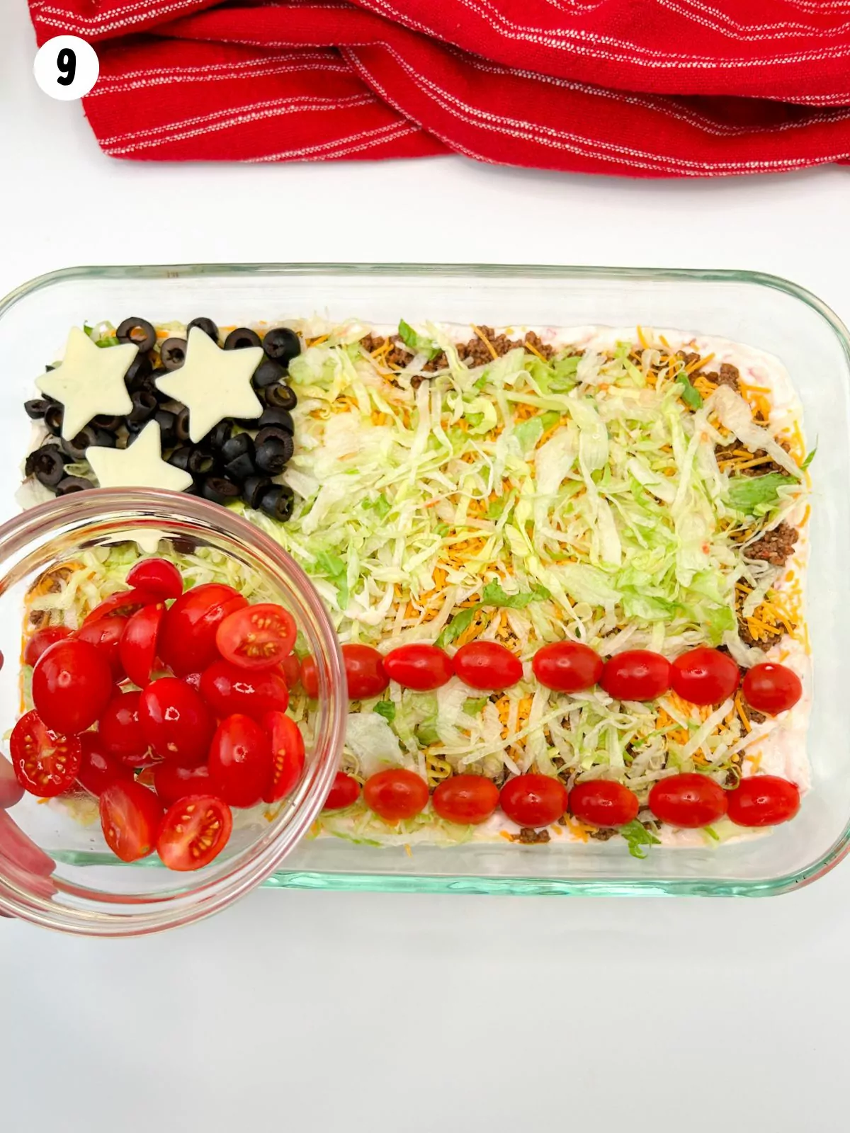 grape tomatoes in small bowl being held over American flag themed taco dip.