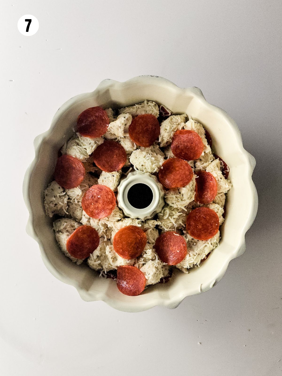 overhead view of bundt pan with refrigerator biscuits cut up with cheese, pepperoni and spices.