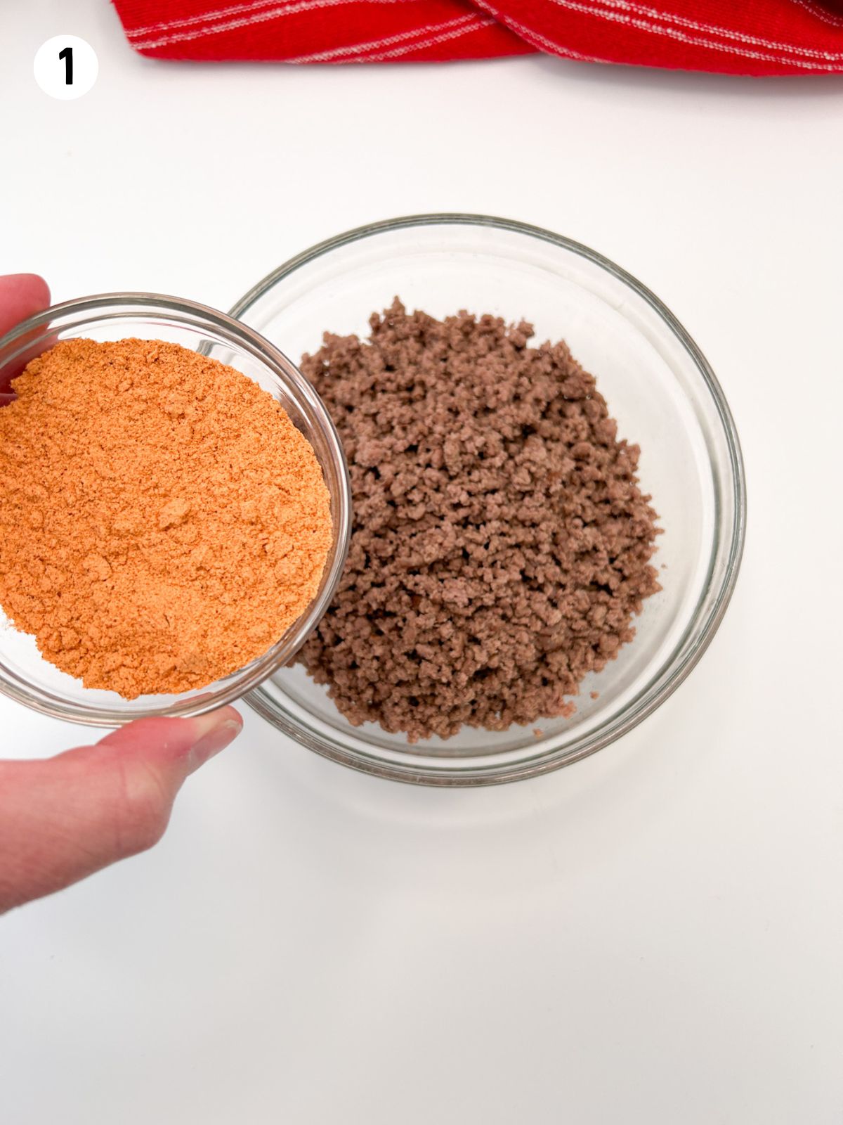 small bowl of seasoning being added to cooked ground beef.