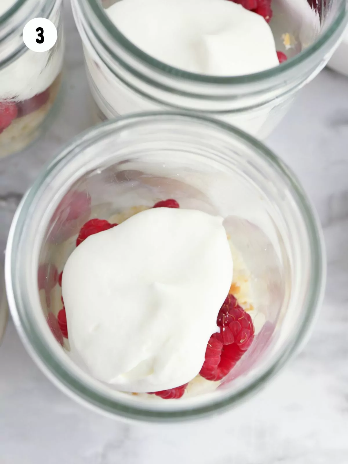 overhead view of whipped cream on top of raspberries in mason jar.