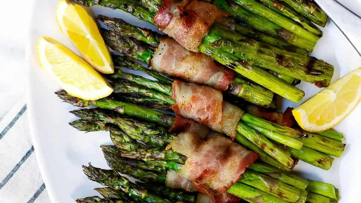 Bundles of asparagus wrapped in bacon with a lemon wedge nearby.