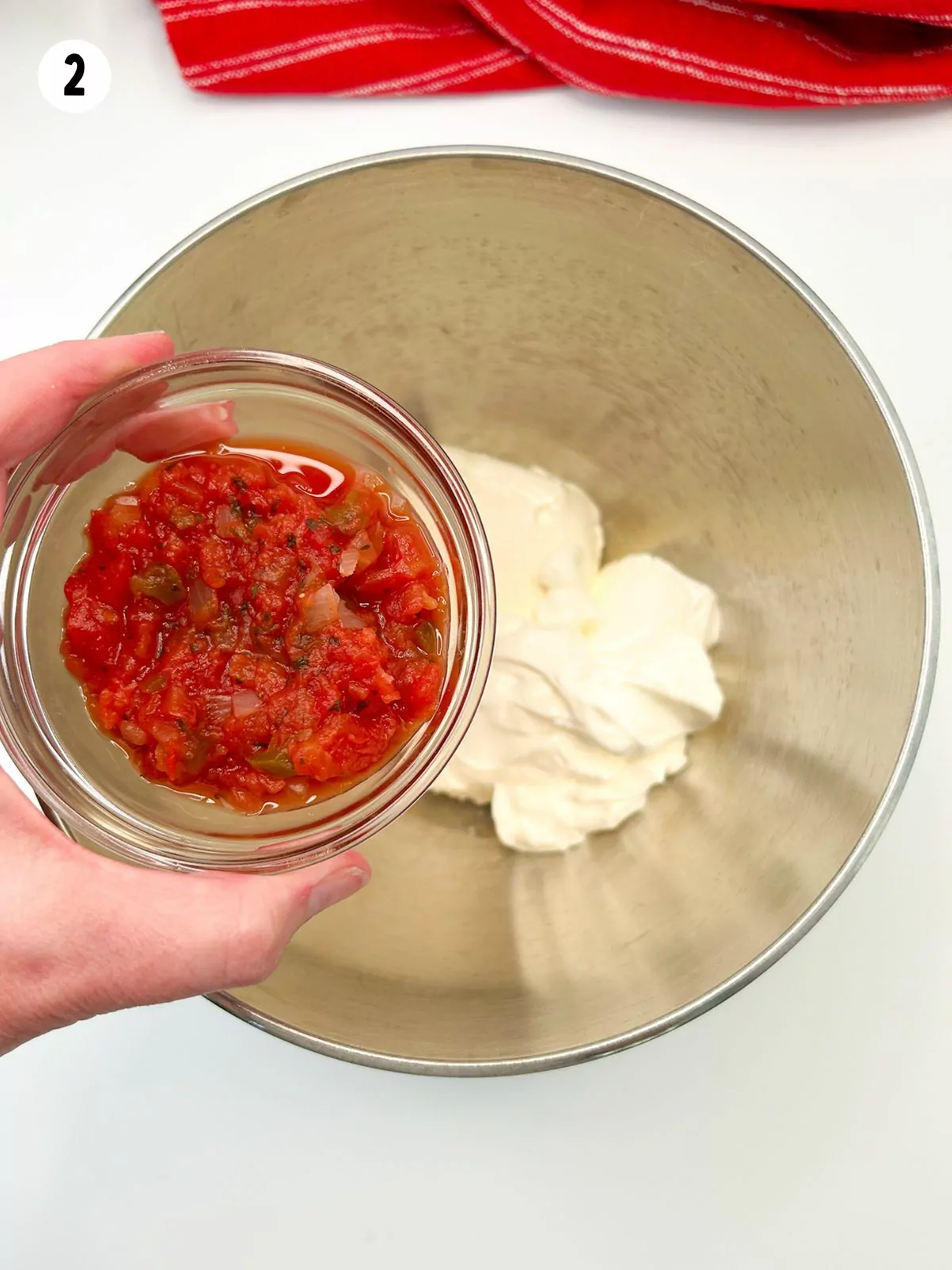 small bowl of salsa being held over mixing bowl with sour cream and cream cheese.