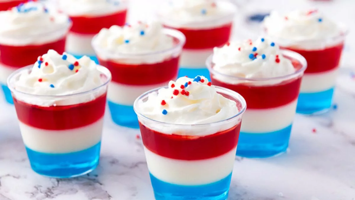 Layered jello cups in red, white and blue with whipped cream and sprinkles.