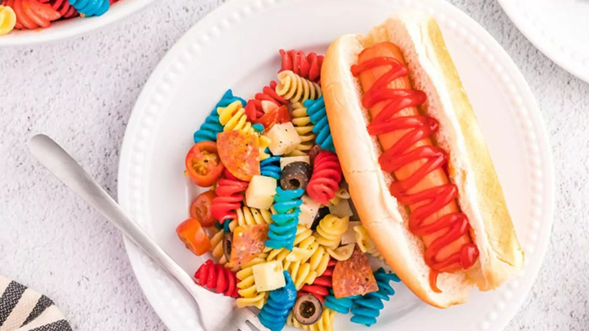 Patriotic pasta salad on a plate with a hot dog.