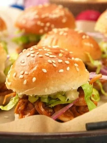 a tray of saucy pulled pork sliders with slaw.