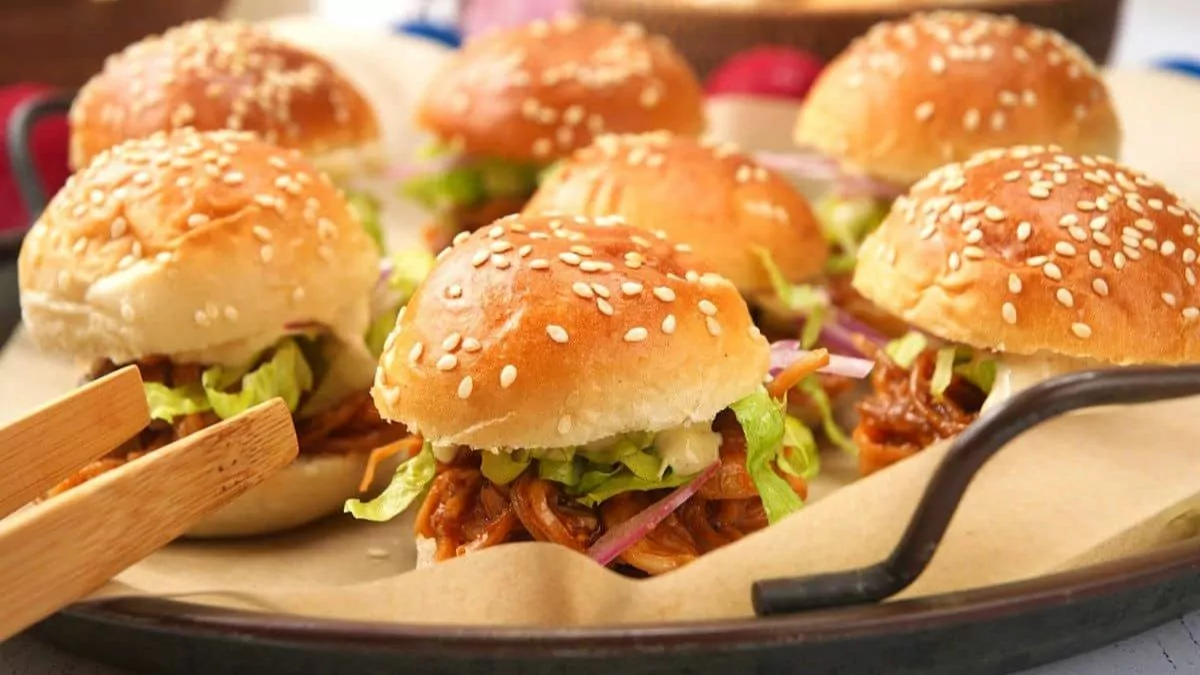 a tray of saucy pulled pork sliders with slaw.