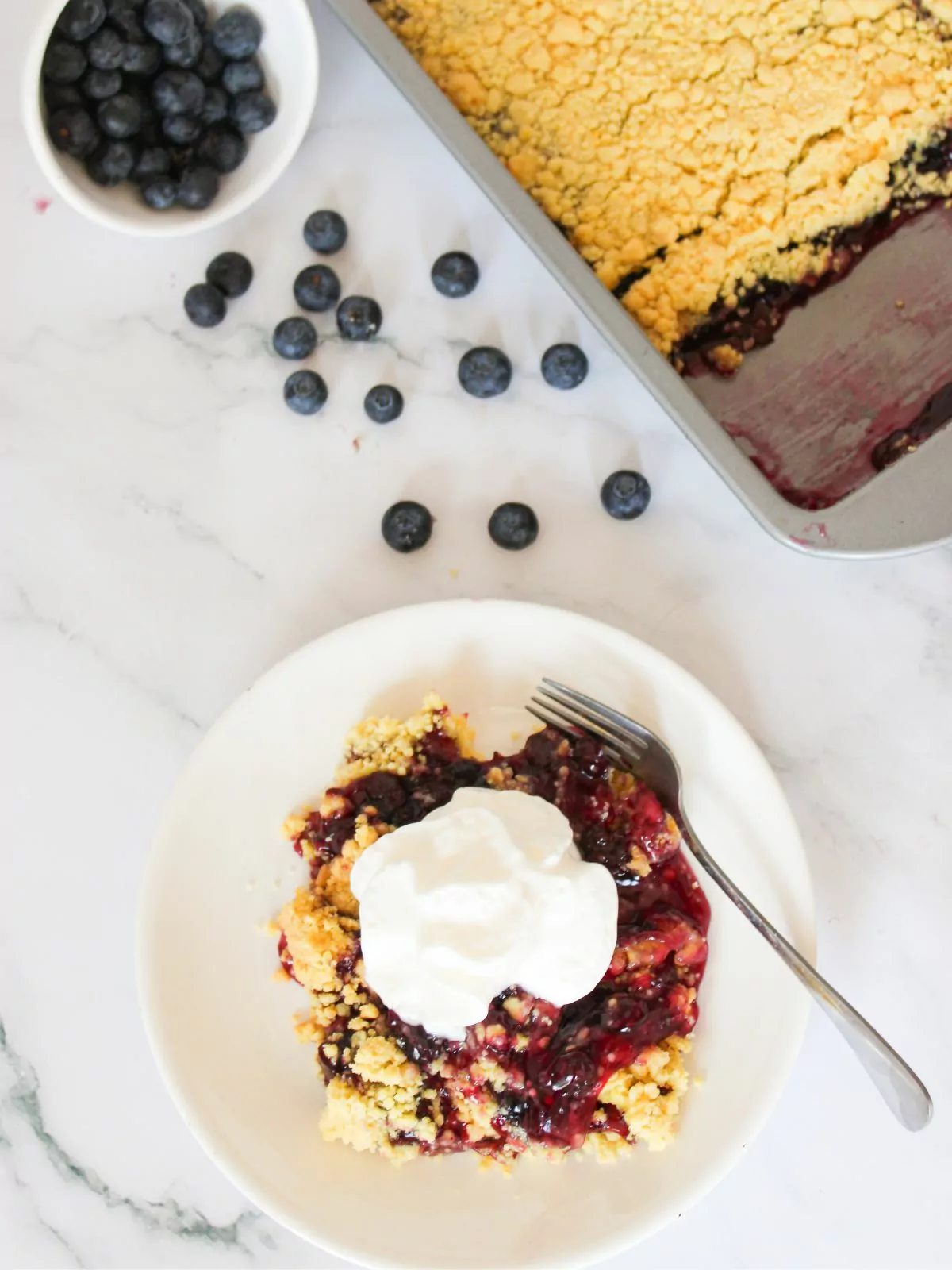 blueberry dump cake served on plate with whipped cream.