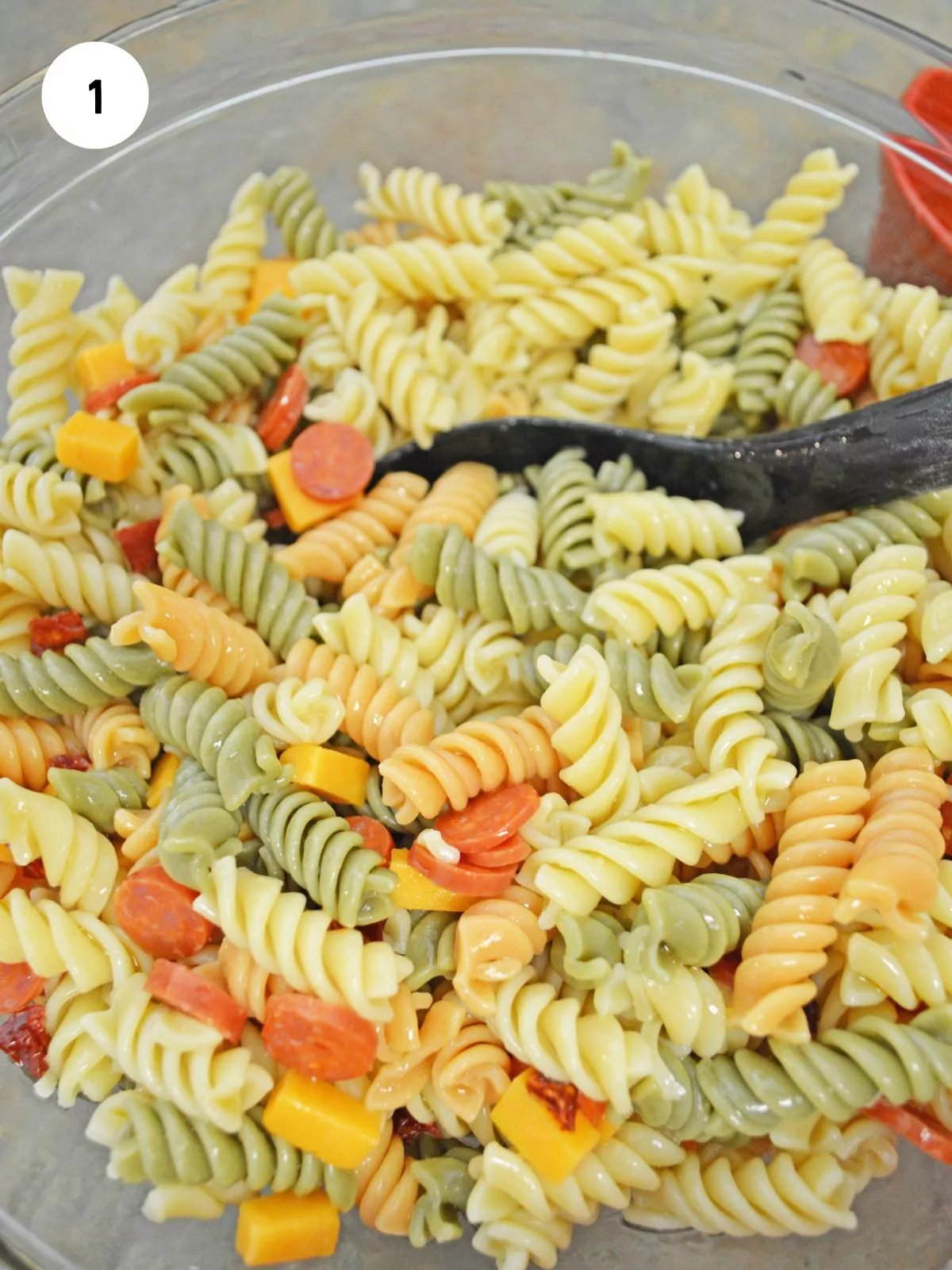 tri color pasta, mini pepperoni, cheese cubes mixed together in a clear bowl