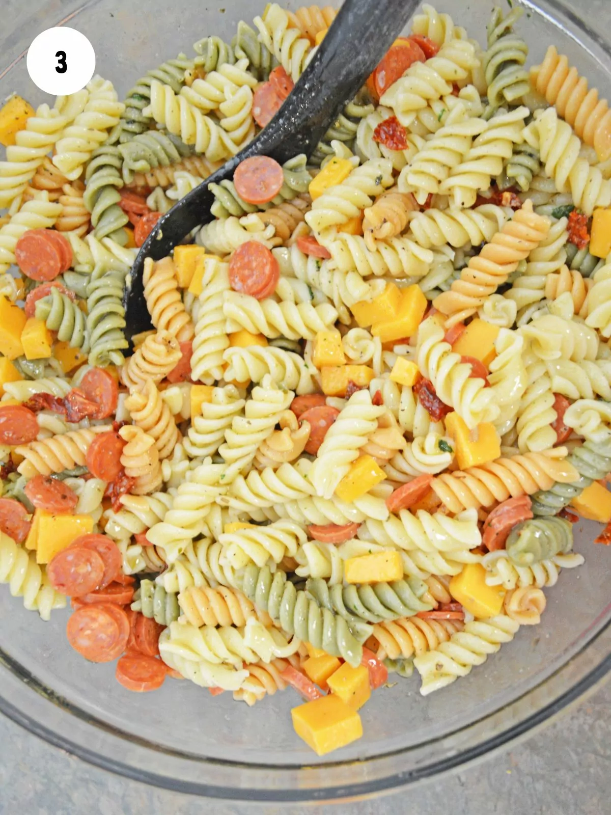 pasta salad being mixed in a clear bowl.