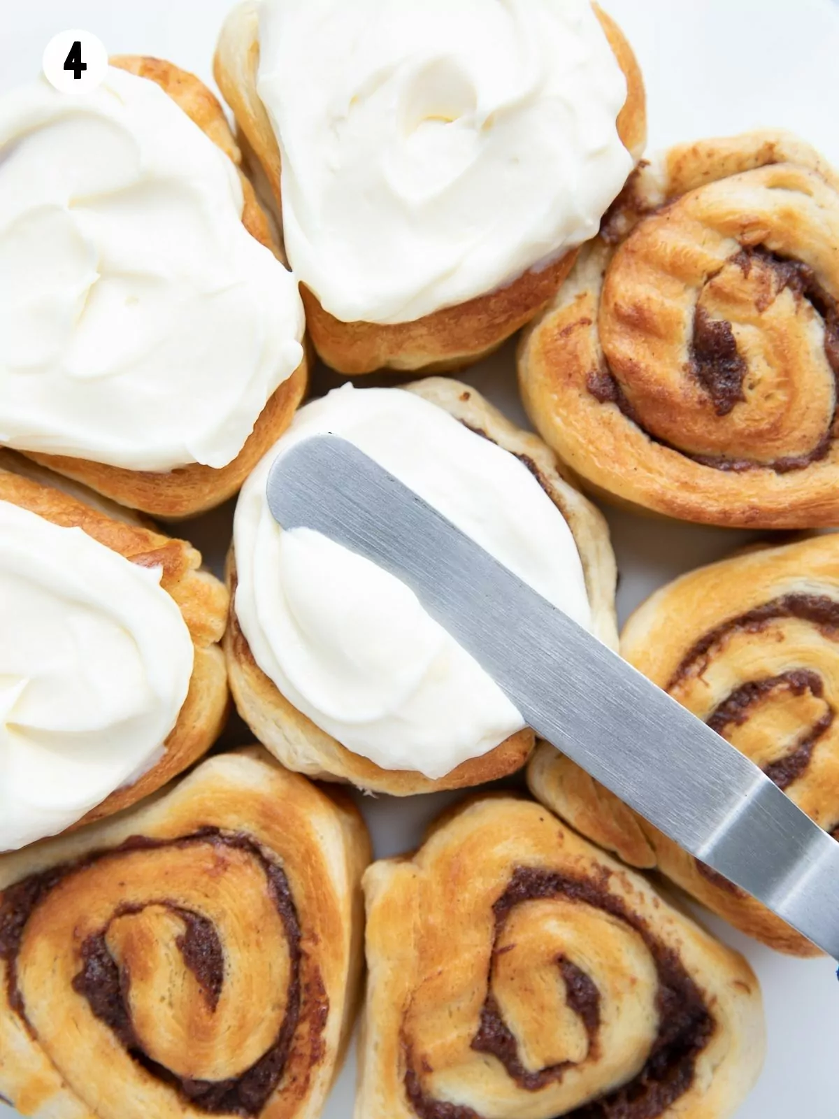 cinnamon rolls being frosted with a small offset spatula