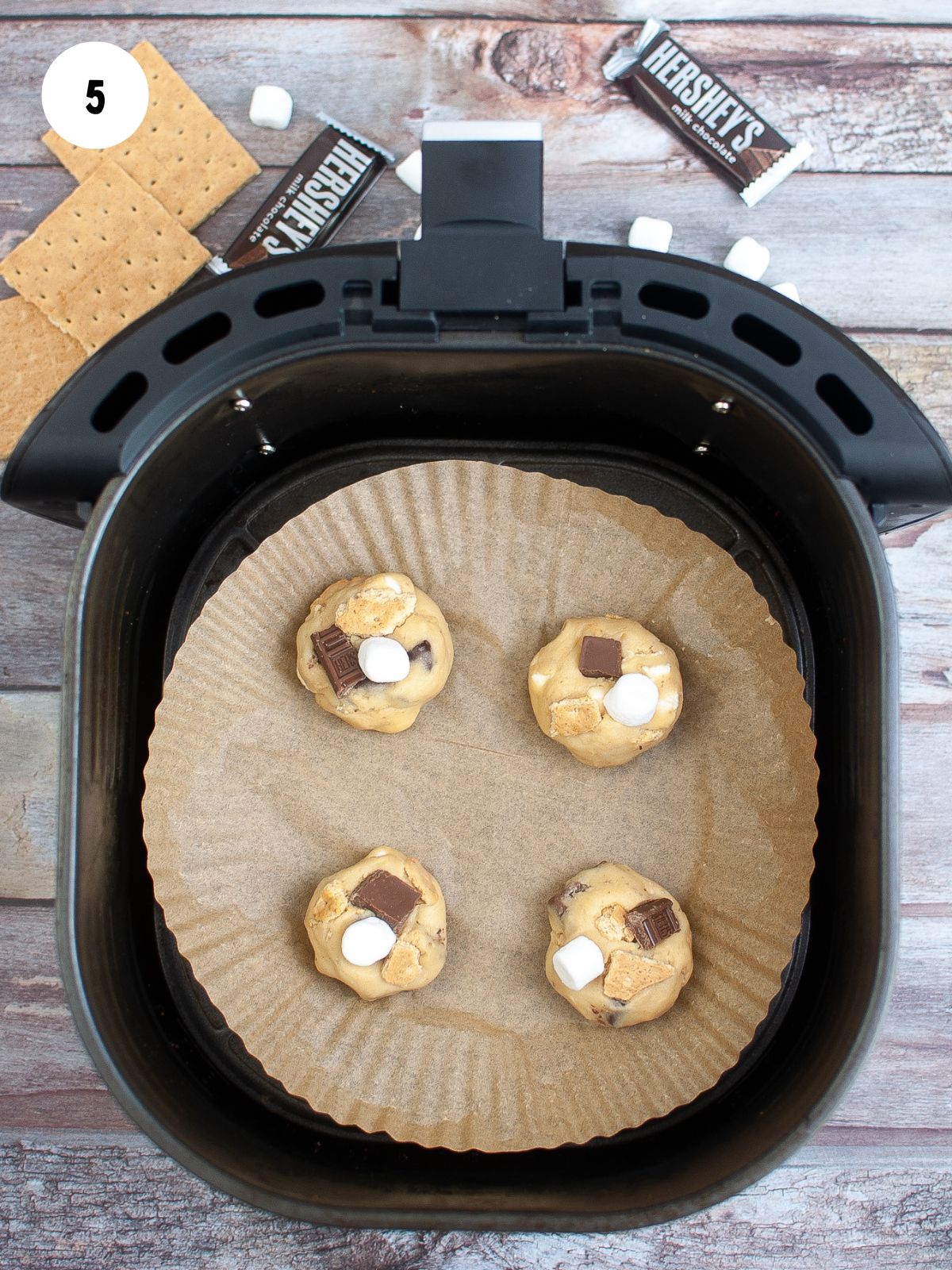 Scoops of cookie dough on parchment paper placed in the air fryer basket