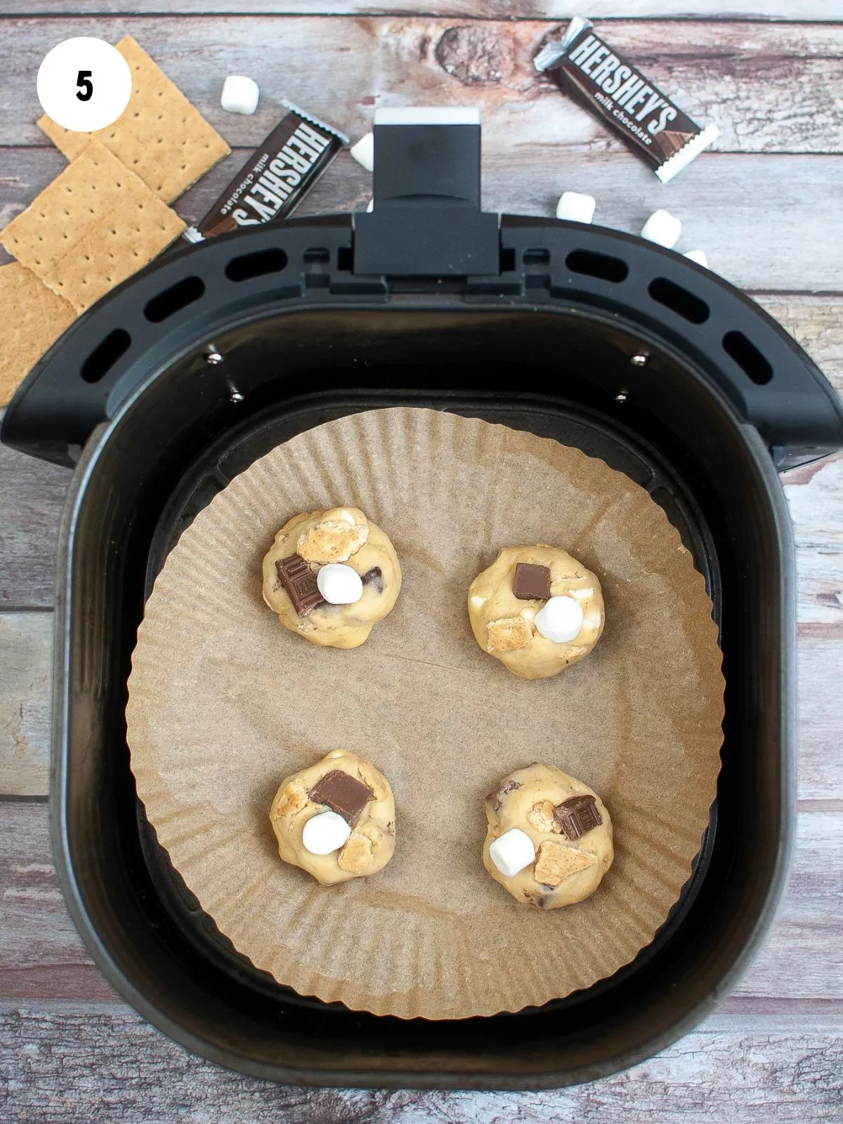 Scoops of cookie dough on parchment paper placed in the air fryer basket