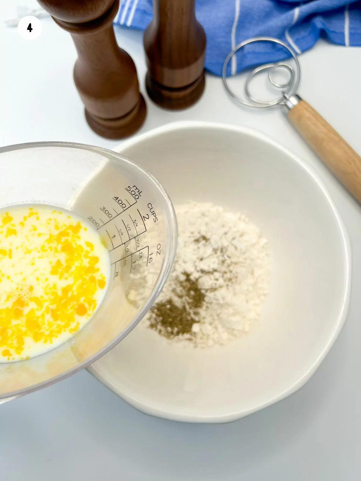 eggs and milk in measuring cup over bowl with dry ingredients.