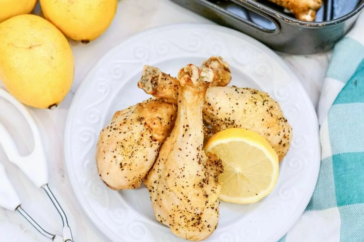 baked drumsticks on white plate with lemon slices.