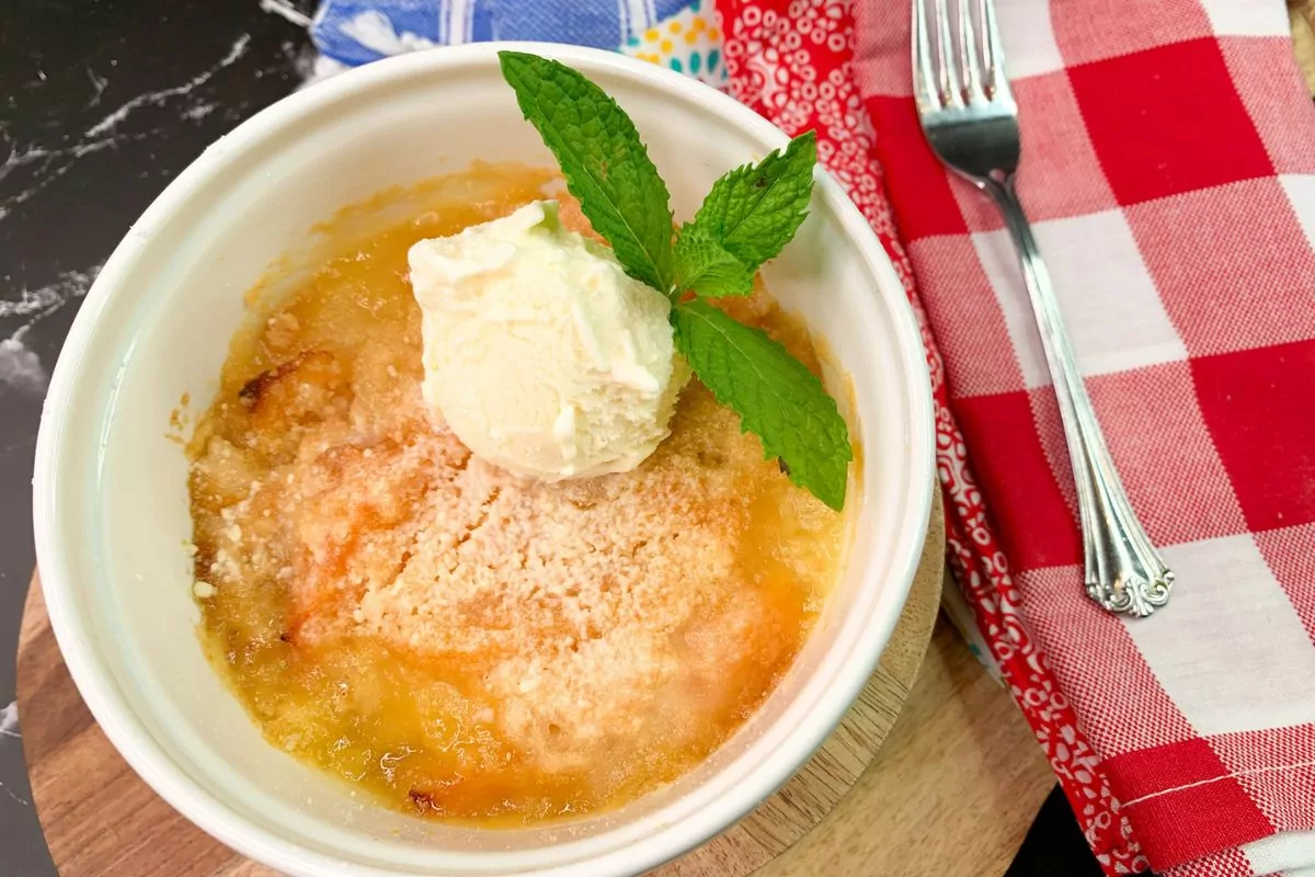 Baked peach cake in small white dish with scoop of vanilla ice cream and a sprig of mint.