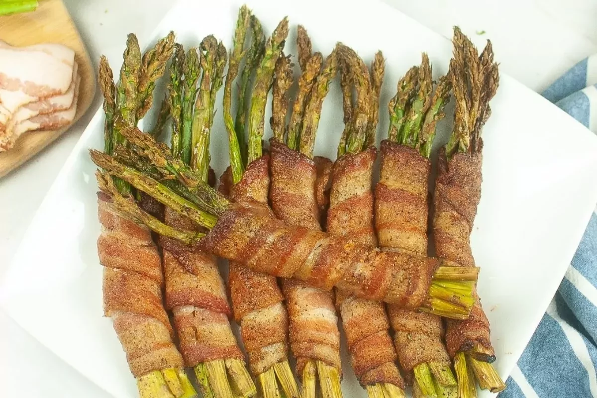 A white plate filled with golden brown bacon-wrapped asparagus spears, ready to be enjoyed as a delicious appetizer or side dish.
