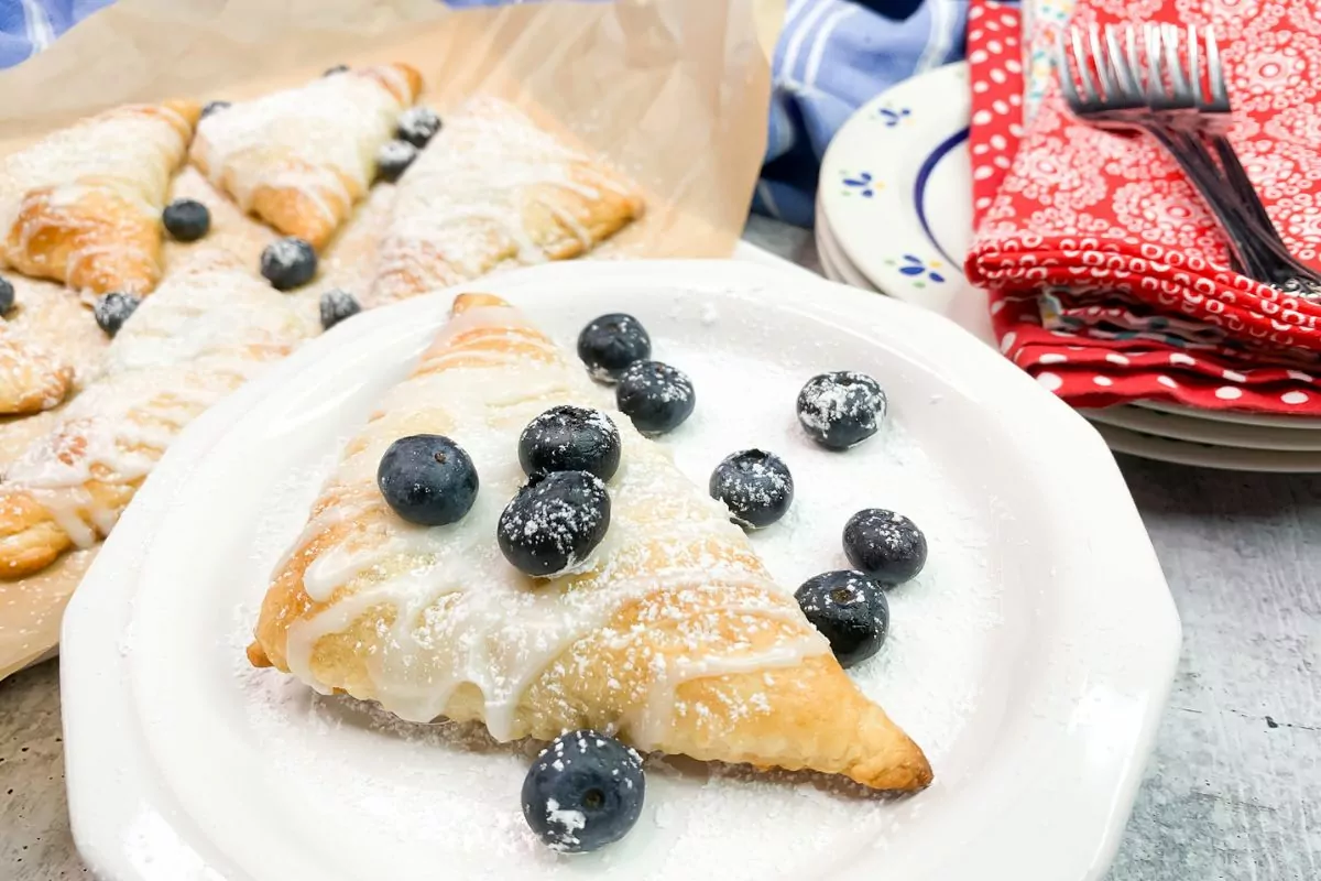 blueberry turnover on white plate with more in the background on a baking tray.