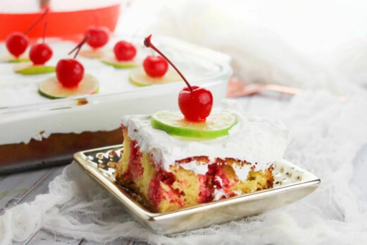 A slice of cake with red and green ribbons throughout; topped with cherries and a lime slice.