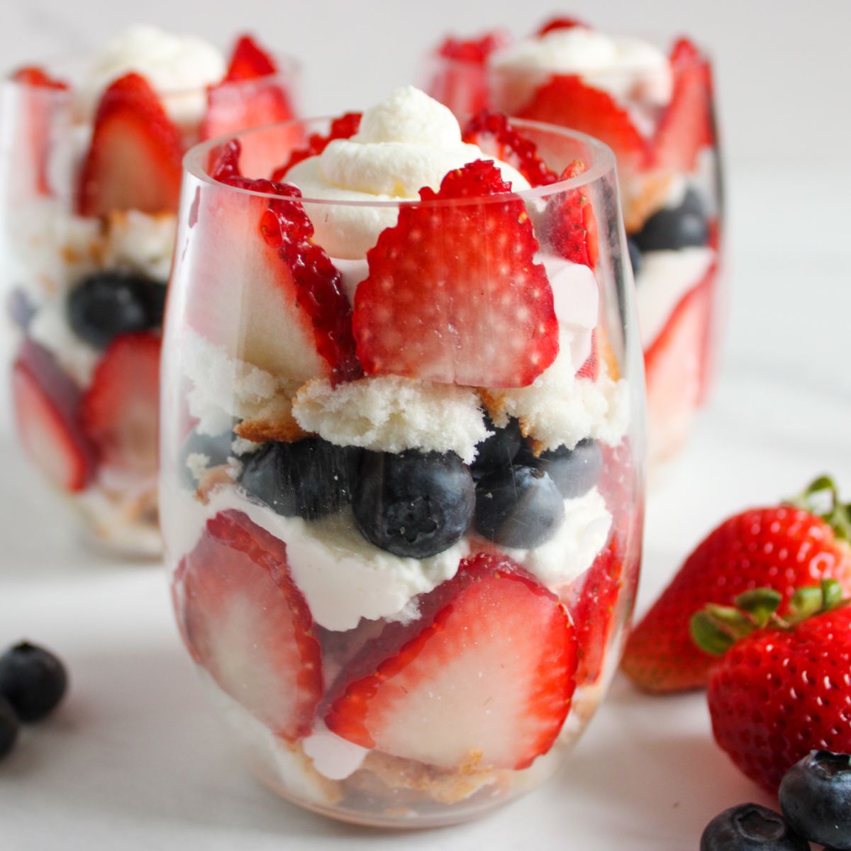 glass filled with strawberries, blueberries, whipped cream and angel food cake.