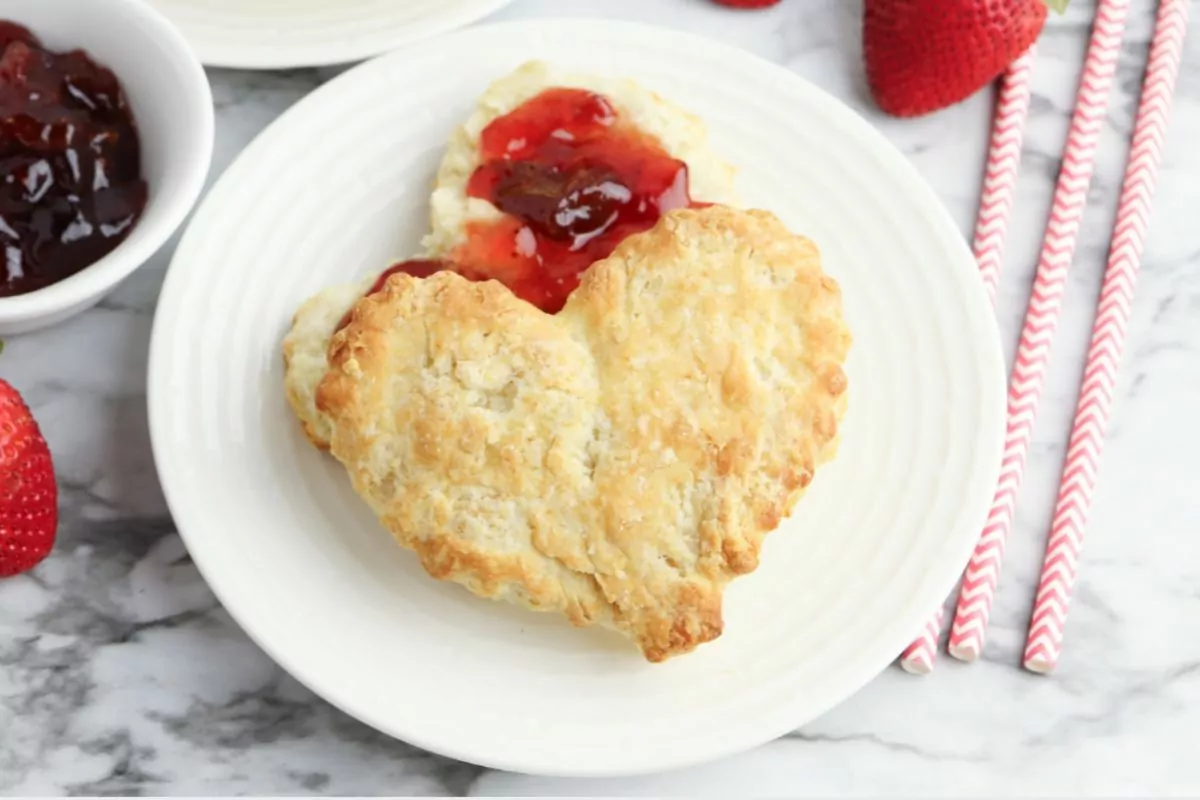 A plate of warm, heart-shaped homemade biscuits, freshly baked and ready to be enjoyed with butter and jam.