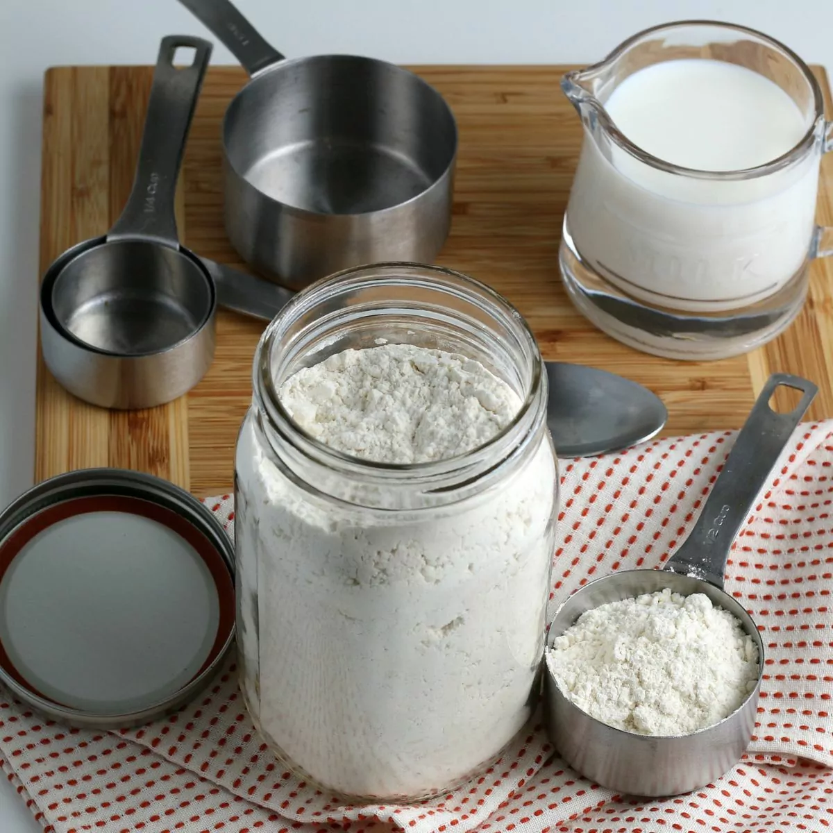 Homemade Bisquick mix in mason jar and measuring cup with small pitcher of milk in background.