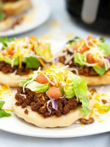 Three fry bread tacos on a plate with lettuce, tomato and cheese over the top.